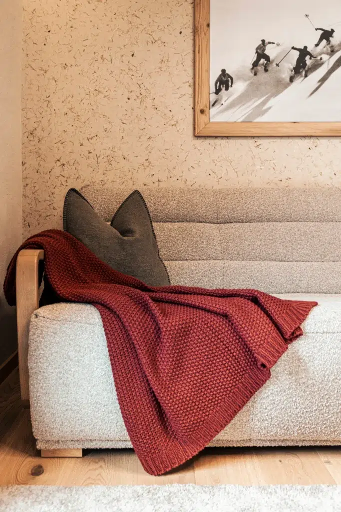 Cozy apartment sofa with a red knit blanket, gray pillow, and skiing photo above.